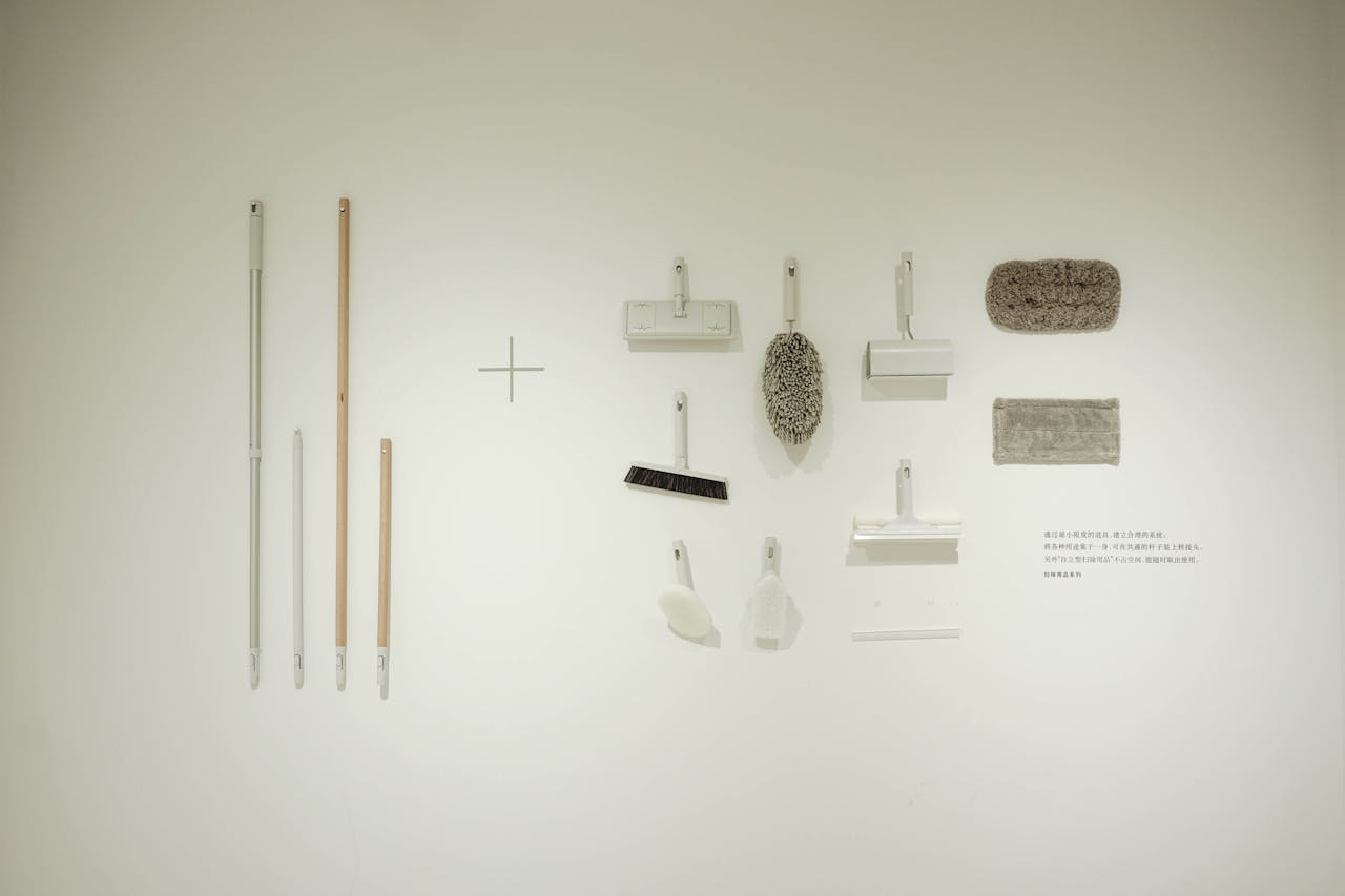 A minimalist flat lay of various cleaning tools arranged on a white wall, showcasing a modern concept.
